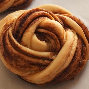 Puede incluir: Primer plano de un rollo de canela con un diseño en espiral. El rollo es de color marrón dorado y tiene un acabado brillante.