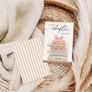May include: A baby shower invitation card with the text "A New Chapter Begins" and a stack of books with a pink bow. The invitation is on a woven tray with a striped card and a fluffy beige blanket.