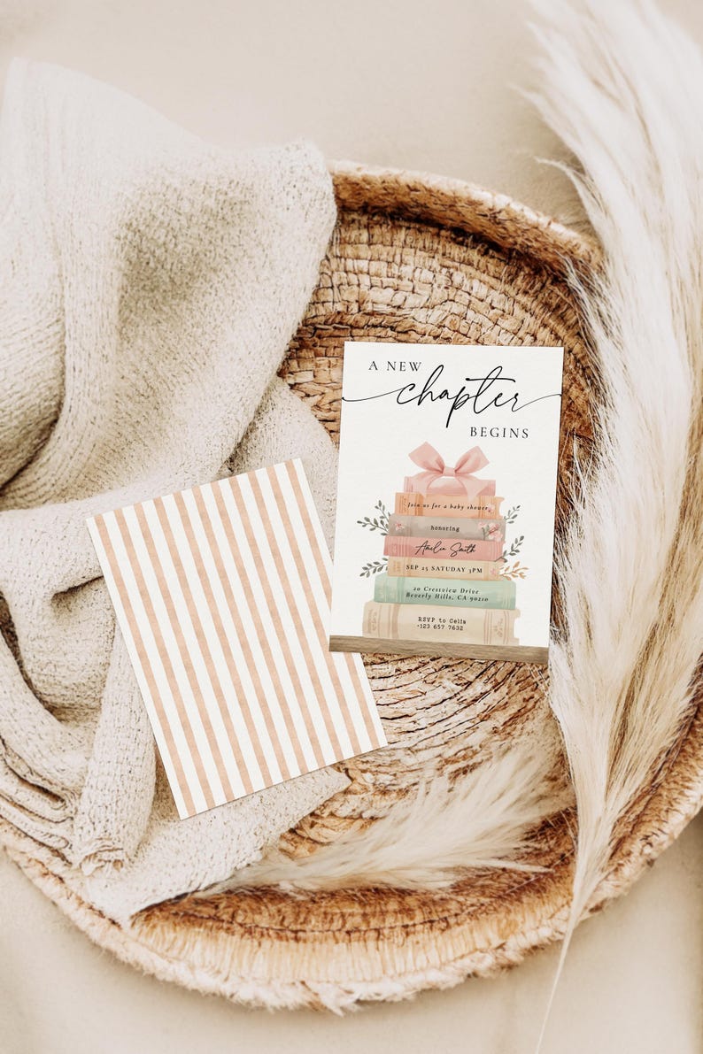 May include: A baby shower invitation card with the text "A New Chapter Begins" and a stack of books with a pink bow. The invitation is on a woven tray with a striped card and a fluffy beige blanket.