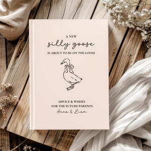 Op de afbeelding: Een lichtroze baby-adviesboek met de tekst "A New Silly Goose Is About To Be On The Loose." Onder de tekst staat een lijntekening van een gans met een strik. Het boek is voor "Advice & Wishes For The Future Parents Anna & Liam."