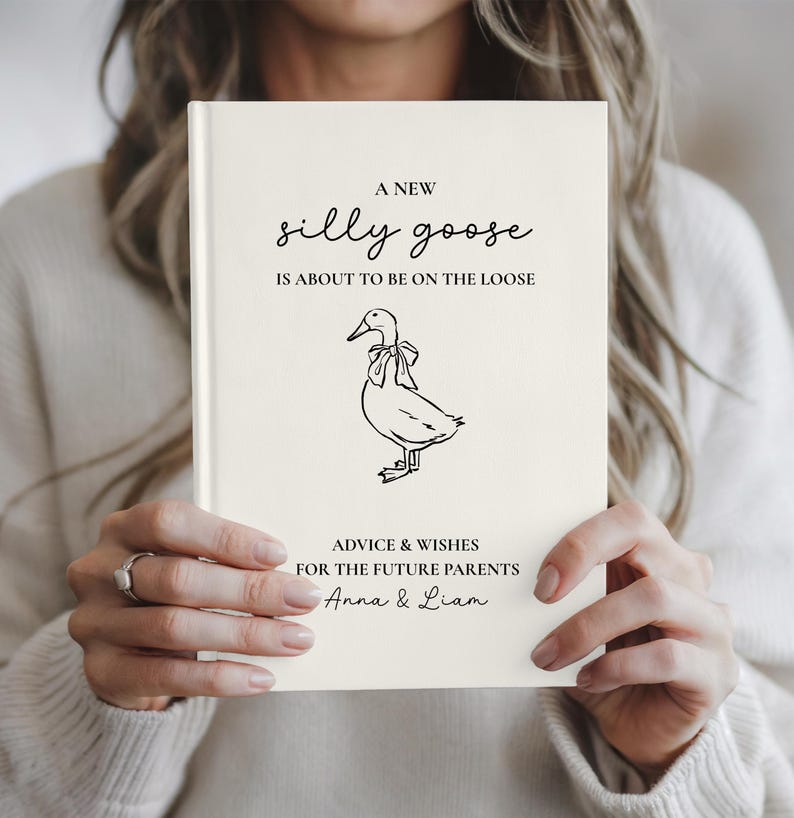 May include: A cream-colored book with the text 'A NEW silly goose IS ABOUT TO BE ON THE LOOSE' in black script. Below is a black and white illustration of a duck with a bow. The text 'ADVICE & WISHES FOR THE FUTURE PARENTS Anna & Liam' is at the bottom.
