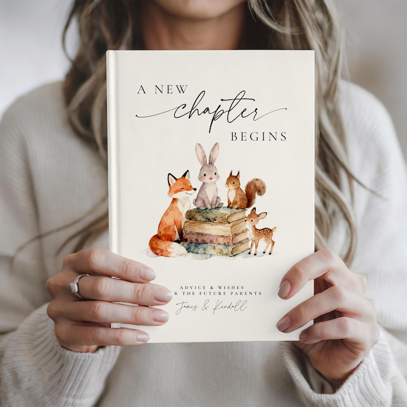 May include: A cream-colored book with the text "A New Chapter Begins" in elegant script. The cover features watercolor illustrations of a fox, rabbit, squirrel, and deer. The book is labeled "Advice & Wishes for the Future Parents" with names below.