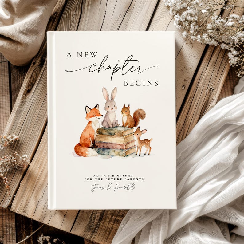 May include: A white hardcover book with the text "A New Chapter Begins" and watercolor illustrations of a fox, rabbit, squirrel, and deer. The book is for advice and wishes for future parents, with names below.