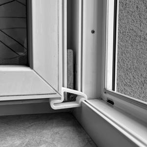 Könnte beinhalten: Nahaufnahme eines weißen Fensterrahmens mit einem Kunststoffverschluss. Das Fenster ist teilweise geöffnet und gibt einen Blick auf die Außenwand frei. Der Rahmen ist sauber und modern gestaltet.