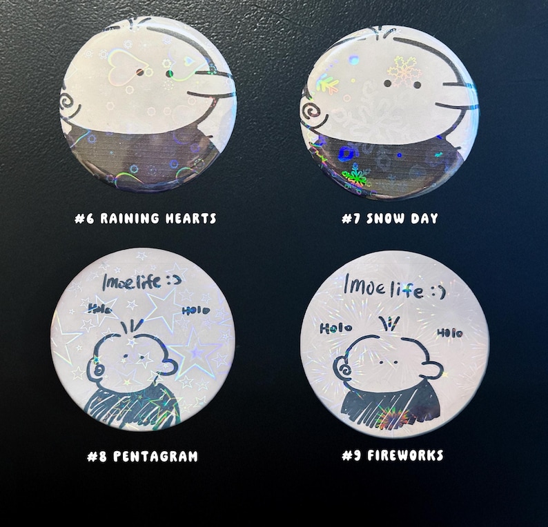 Op de afbeelding: Vier ronde, witte knopen met cartoon illustraties en tekst. Twee knopen hebben een ontwerp van een gezicht met de tekst "#6 RAINING HEARTS" en "#7 SNOW DAY". De andere twee knopen hebben een gezichtsontwerp met de tekst "#8 PENTAGRAM" en "#9 FIREWORKS".