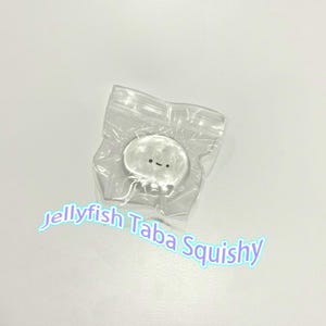 Può includere: Un giocattolo squishy trasparente a forma di medusa con un volto sorridente, confezionato in un sacchetto di plastica trasparente. Il testo "jellyfish Taba Squishy" è scritto in blu chiaro brillante.