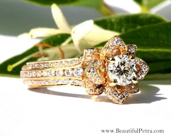 May include: A gold engagement ring with a large, round, clear diamond center stone. The ring features a floral design with smaller diamonds surrounding the center stone and along the band. The website address www.BeautifulPetra.com is visible.