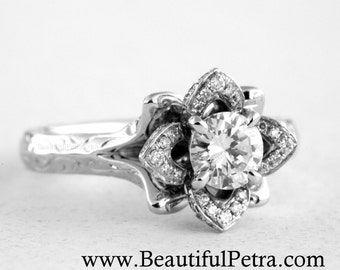 May include: A silver engagement ring with a floral design. The ring features a large, round, clear gemstone at the center, surrounded by smaller, sparkling stones. The band has a textured pattern. The website address www.BeautifulPetra.com is visible.