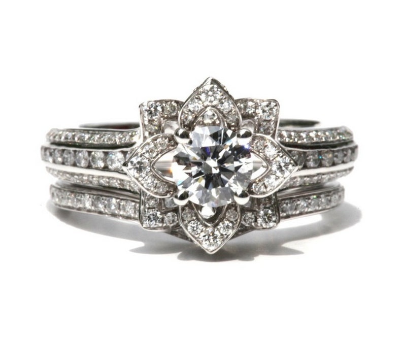 Puede incluir: Un anillo de compromiso de plata con un gran diamante redondo y claro engastado en un halo con forma de flor. El anillo est&aacute; rodeado de diamantes m&aacute;s peque&ntilde;os y tiene una banda a juego.