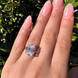 May include: A large oval-shaped diamond engagement ring set in a gold band. The ring is on a person's finger.