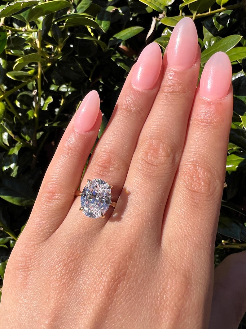 May include: A large oval-shaped diamond engagement ring set in a gold band. The ring is on a person's finger.