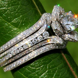 Puede incluir: Un anillo de plata con un gran diamante brillante engastado en un dise&ntilde;o con forma de flor. El anillo est&aacute; rodeado de diamantes m&aacute;s peque&ntilde;os, creando un efecto deslumbrante.