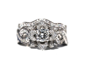 May include: A silver engagement ring with a large, round, center diamond set in a flower-shaped design. The band is adorned with smaller diamonds and has a delicate, intricate design.