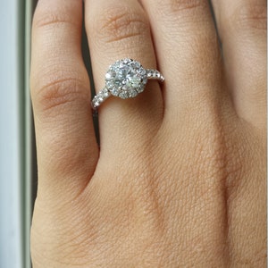Op de afbeelding: Een zilveren ring met een grote, ronde, heldere diamant omgeven door een halo van kleinere diamanten.