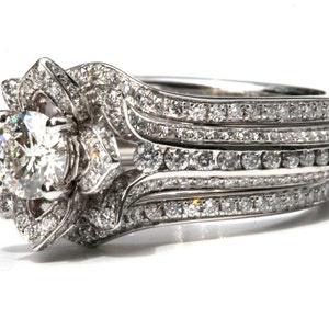 Puede incluir: Un anillo de compromiso de plata con un gran diamante redondo central rodeado de diamantes m&aacute;s peque&ntilde;os. La banda est&aacute; adornada con varias filas de diamantes m&aacute;s peque&ntilde;os.