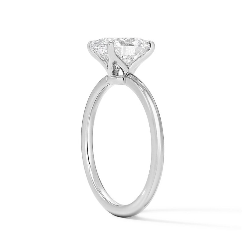 May include: A simple solitaire engagement ring with a round brilliant cut diamond set in a four-prong setting. The band is a thin, polished, and smooth platinum band.