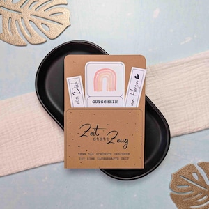 Könnte beinhalten: Ein brauner Geschenkkartenhalter aus Papier mit dem Text "Zeit statt Zeug" und "Denn das schönste Geschenk ist eine zauberhafte Zeit." Im Inneren befinden sich Karten mit einem Regenbogen, den Wörtern "Für Dich" und "von Herzen."