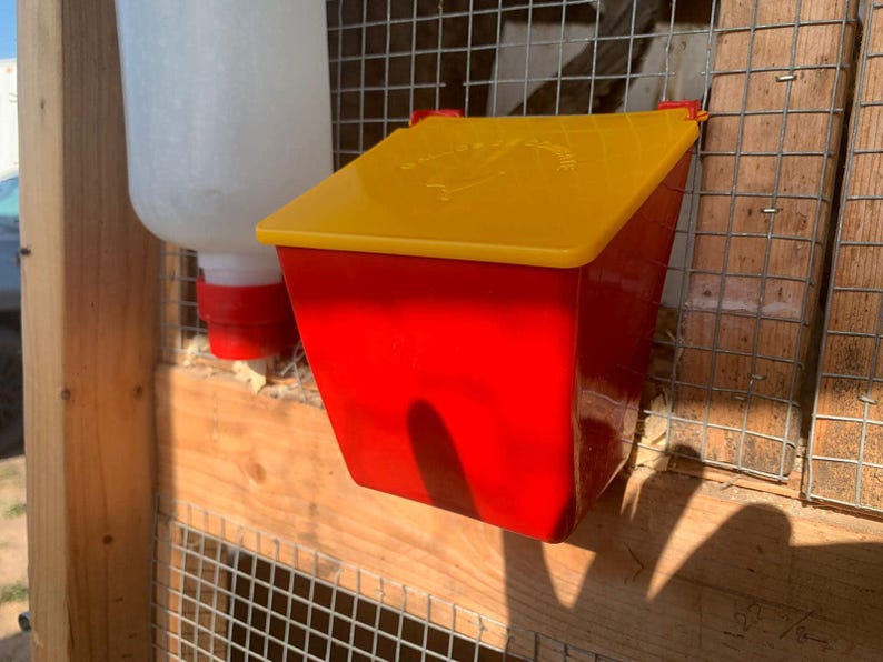May include: Red and yellow plastic chicken feeder with a hinged lid. The feeder has a white plastic bird silhouette on the lid with the text "Chickens & Roosters".