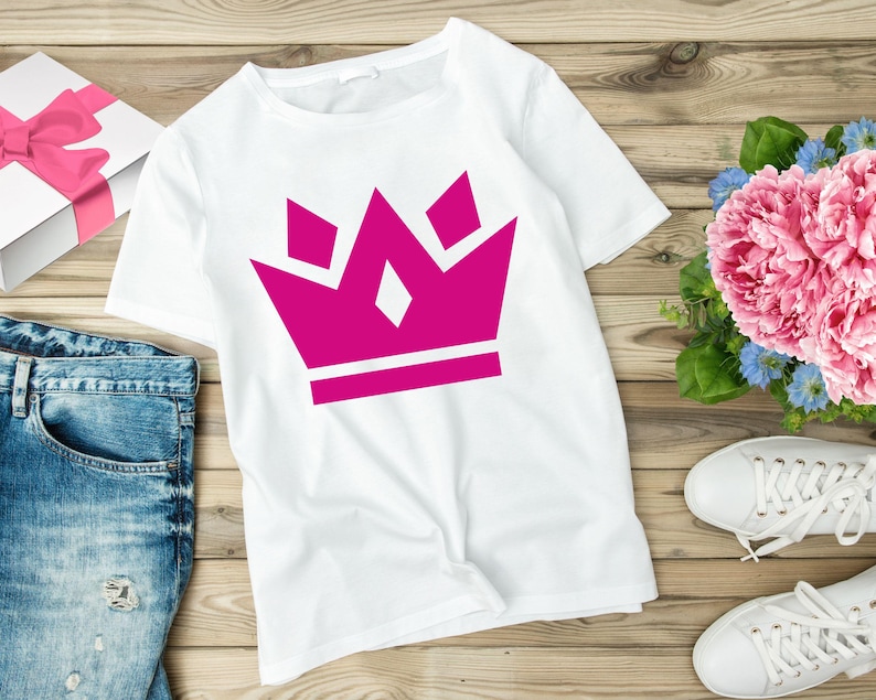 May include: White t-shirt with a pink crown graphic. The crown is made up of five points and has a white outline.