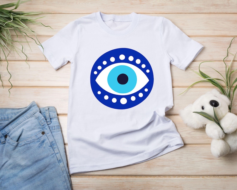 May include: White t-shirt with a blue evil eye design. The eye is surrounded by a circle of white dots.
