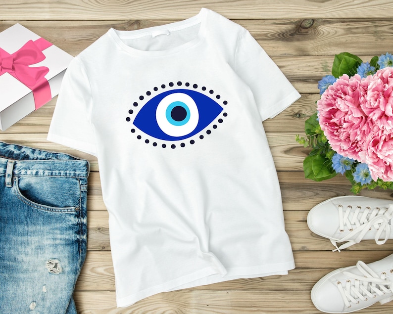 May include: White t-shirt with a blue and white evil eye design. The evil eye is a symbol of protection against negative energy.