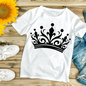 May include: White t-shirt with a black crown graphic design. The crown has a detailed ornate design with a pointed top and a thick band.