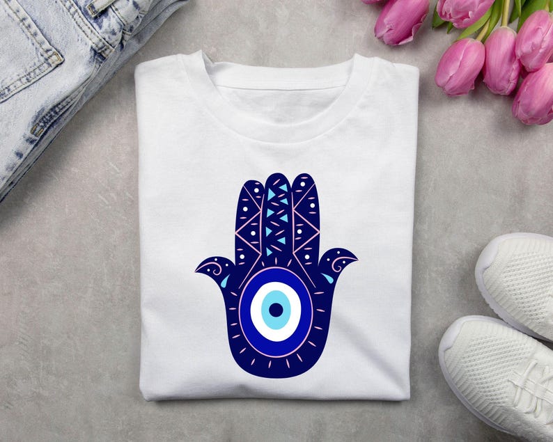 May include: White t-shirt with a blue and white hamsa hand design. The hamsa hand has a blue evil eye in the center.