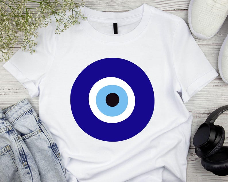 May include: White t-shirt with a blue evil eye design. The eye is surrounded by a white circle and a blue circle.