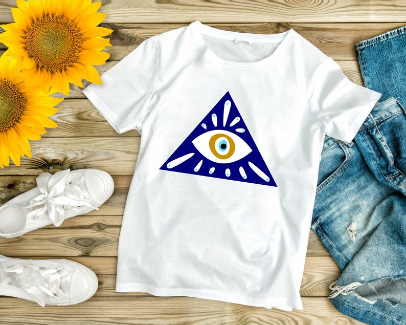 May include: White t-shirt with a blue triangle and a white eye with a blue pupil and a gold iris. The eye is surrounded by white rays.