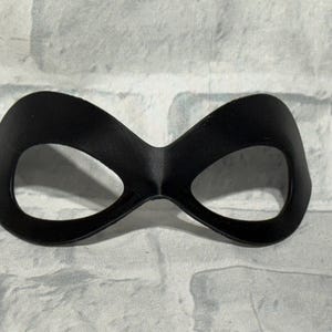 Puede incluir: Una m&aacute;scara de ojos negra con un dise&ntilde;o curvo. La m&aacute;scara tiene dos grandes aberturas para los ojos y est&aacute; hecha de un material liso y mate. La m&aacute;scara est&aacute; dise&ntilde;ada para cubrir el &aacute;rea alrededor de los ojos.