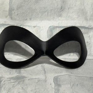Puede incluir: Una m&aacute;scara de ojos negra con un dise&ntilde;o curvo. La m&aacute;scara tiene dos grandes aberturas para los ojos y est&aacute; hecha de un material liso y mate. La m&aacute;scara est&aacute; dise&ntilde;ada para cubrir los ojos y el &aacute;rea que los rodea.