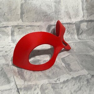 Puede incluir: Una m&aacute;scara de ojos roja brillante con un dise&ntilde;o curvo y una parte superior puntiaguda. La m&aacute;scara tiene una gran abertura ovalada para el ojo y est&aacute; hecha de un material liso y s&oacute;lido. Probablemente para disfraces o uso teatral.