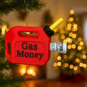 Può includere: Ornamento natalizio a forma di tanica di benzina rossa con la scritta nera "Gas Money". L'ugello è giallo e nero. Una banconota arrotolata è inserita nell'ugello. L'ornamento è appeso a un albero di Natale.