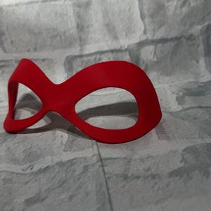 Puede incluir: Una m&aacute;scara para los ojos de color rojo brillante con un dise&ntilde;o curvo. La m&aacute;scara tiene dos grandes aberturas para los ojos y un puente para la nariz. Hecha de un material liso, probablemente para disfraces o para dormir. El dise&ntilde;o es simple pero llamativo.
