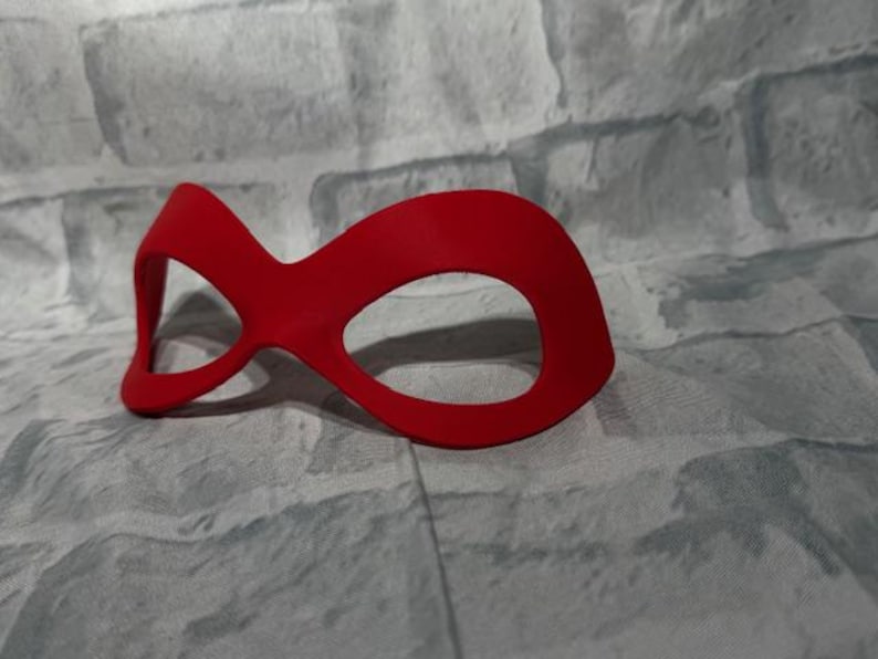 Puede incluir: Una m&aacute;scara para los ojos de color rojo brillante con un dise&ntilde;o curvo. La m&aacute;scara tiene dos grandes aberturas para los ojos y un puente para la nariz. Hecha de un material liso, probablemente para disfraces o para dormir. El dise&ntilde;o es simple pero llamativo.