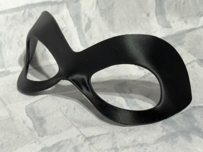 Puede incluir: Una m&aacute;scara de ojos negra con un dise&ntilde;o curvo. La m&aacute;scara tiene dos aberturas para los ojos y est&aacute; hecha de un material liso y mate. La m&aacute;scara est&aacute; dise&ntilde;ada para cubrir los ojos y el puente de la nariz.