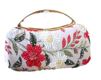 Könnte beinhalten: Weiße Clutch mit goldenem Griff, verziert mit gestickten roten und weißen Blumen, grünen Blättern und Pailletten. Das florale Design bedeckt die Vorder- und Seiten des Beutels und schafft ein dekoratives Accessoire.