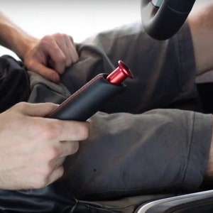 May include: A black leather manual handbrake with a red lever. The handbrake is in a car with a black leather interior and a red stitching detail.