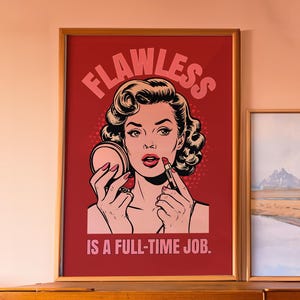 May include: A framed poster with a red background and a black and white illustration of a woman applying lipstick. The text on the poster reads "Flawless is a full-time job."