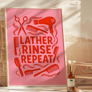 May include: A framed pink poster with red hair styling tools and the text "LATHER RINSE REPEAT". The image includes a hairdryer, scissors, combs, and a hairbrush. A bottle of wine is in the foreground.