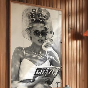 May include: Black and white photo of a woman wearing a hair dryer and sunglasses, reading a magazine called "GRAZIA".