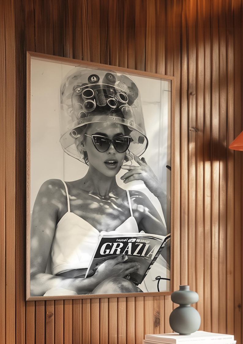 May include: Black and white photo of a woman wearing a hair dryer and sunglasses, reading a magazine called "GRAZIA".