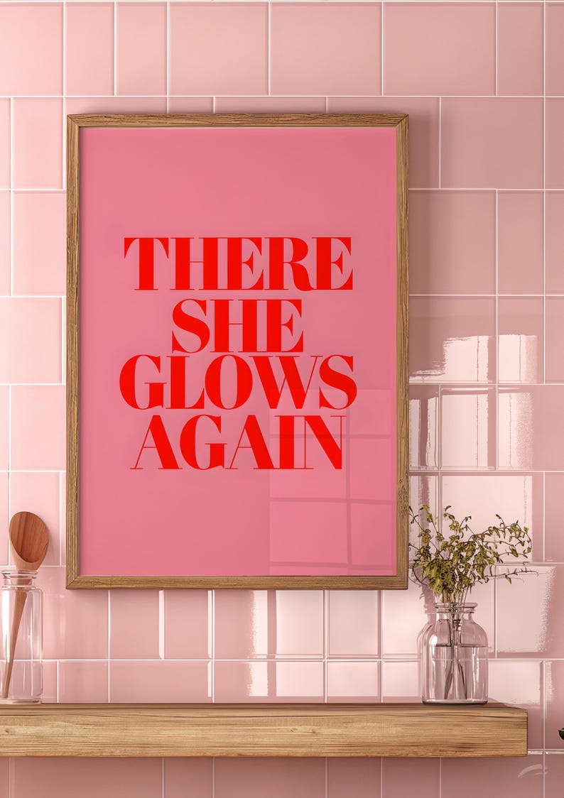 May include: A framed pink poster with the text "THERE SHE GLOWS AGAIN" in red letters.