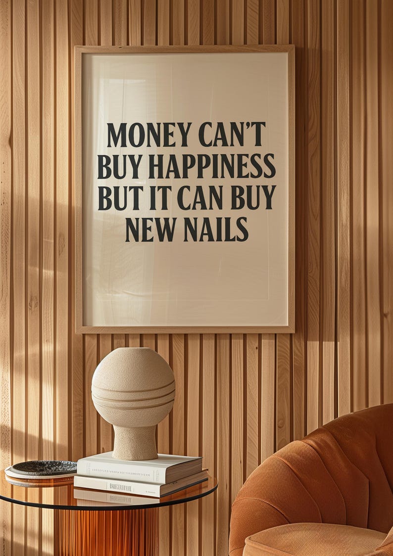 May include: A framed print with the text "MONEY CAN'T BUY HAPPINESS BUT IT CAN BUY NEW NAILS" hangs on a wooden wall. A beige vase with horizontal lines sits on a stack of books on a glass table. An orange chair is in the background.