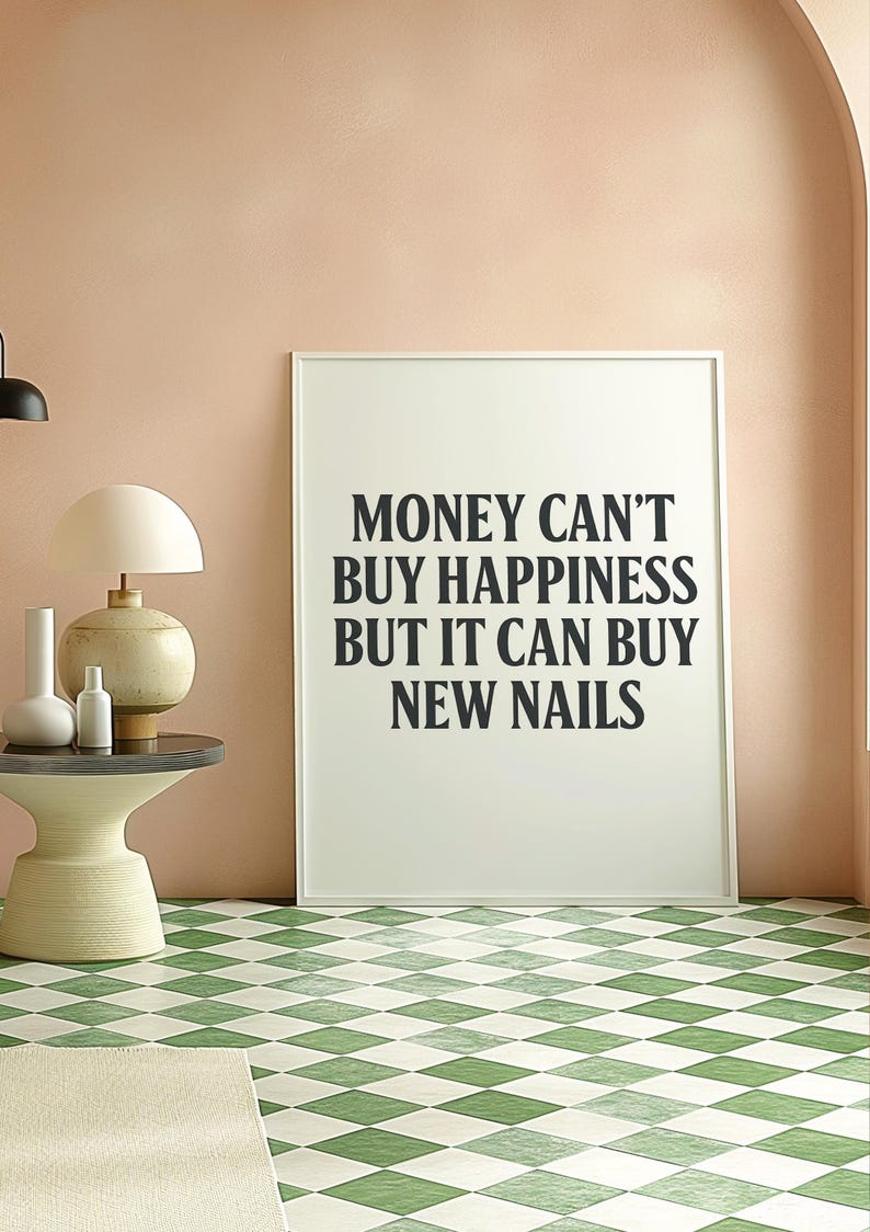 May include: A framed print with the text "MONEY CAN'T BUY HAPPINESS BUT IT CAN BUY NEW NAILS" in black lettering. The print is in a room with a pink wall, a side table with a lamp and vases, and a green and white checkered floor.