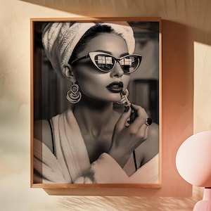 May include: A black and white photograph of a person wearing a white towel on their head and sunglasses. They are applying lipstick with a brush.