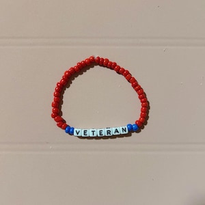 May include: Red, white, and blue beaded bracelet with the word "VETERAN" spelled out in black letters.