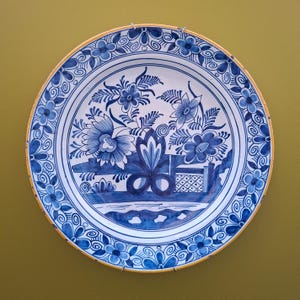Może przedstawiać: Okrągły ceramiczny talerz z białym tłem i skomplikowanymi niebieskimi wzorami kwiatowymi i roślinnymi. Brzeg ozdobiony jest powtarzającym się motywem kwiatowym oraz cienką żółtą obwódką. Centralny wzór przedstawia stylizowane kwiaty i liście.