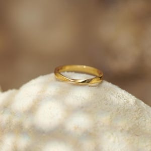 May include: A polished gold ring featuring a continuous twisted band design. The metal surface is smooth and reflective, showcasing a singular elegant twist that creates a subtle, flowing shape around the circumference of the circular band.