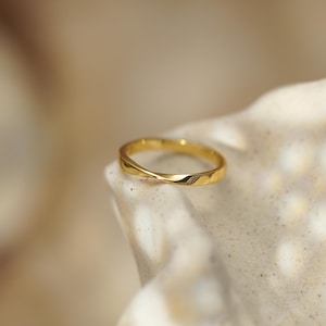 May include: A polished gold ring featuring a smooth, continuous band with a single subtle twist detail. The metal surface is reflective and uniform in color, showcasing a clean, circular design that maintains a consistent width throughout the band.